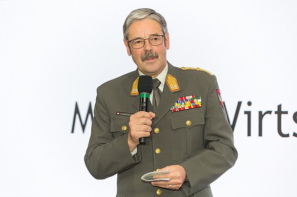 Ein Mann mit Brille und Schnurrbart in Uniform des österreichischen Bundesheeres spricht in ein Mikro.