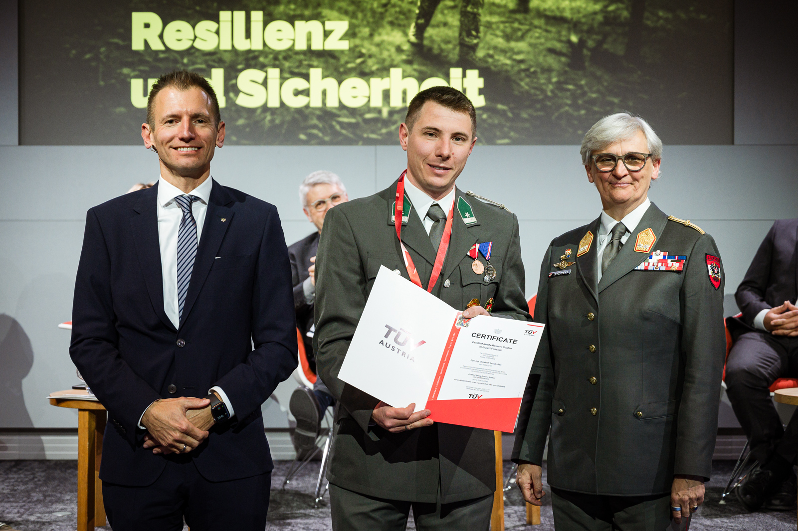 Drei Personen bei Zertifikatsübergabe.